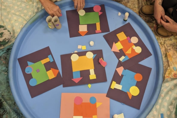 A round table with kids sat around as they make paper-cut trains