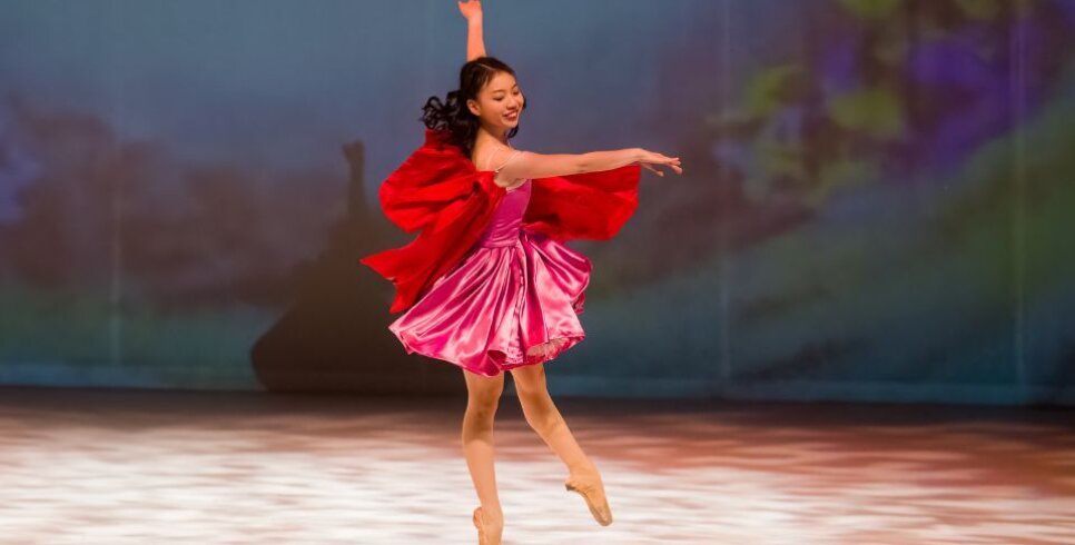 An image from Roald Dahl's Red Riding Hood & The Three Little Pigs at the Corn Exchange Newbury, a ballet dancer playing Red Riding Hood stands up on pointe on one leg, her red dress and cape swish out around her