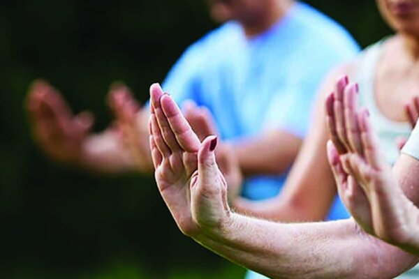 A close-up of 3 pairs of hands holding a tai chi pose with their arms stretched in front, hands upright and palms facing outwards. The first pair of hands are in focus and the other two are blurred in the background.