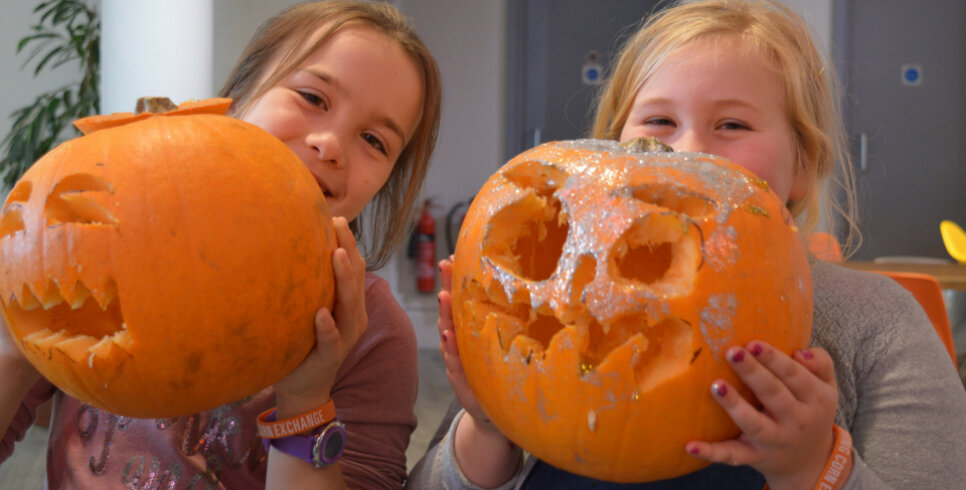 Two young females are smiling and each holding a carved pumpkin.