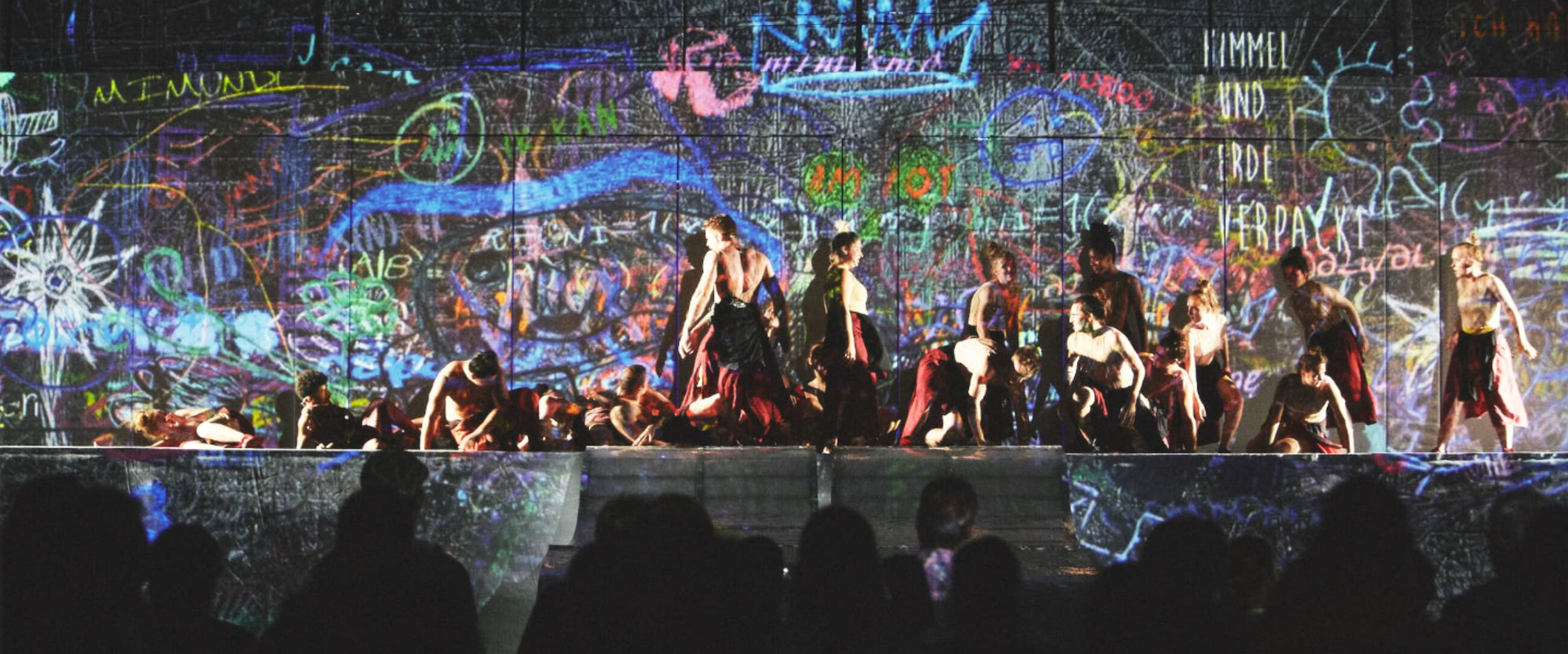 Performing artists in motion on a stage with graffiti backdrop behind them