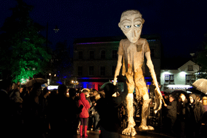 A giant puppet walks through the streets of Newbury, towering above the heads of the crowd.