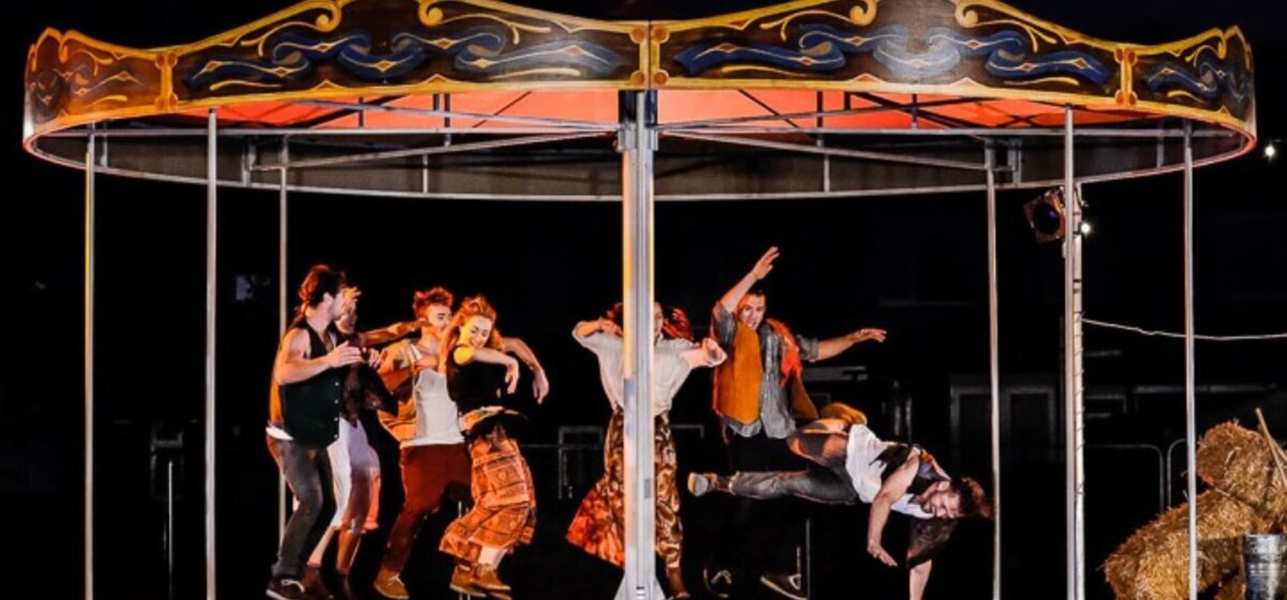 Couples in loose, bohemian, gypsy like clothing dance on a small fairground carousel.