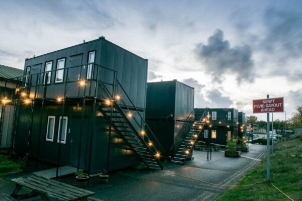 Exterior of 101 cabins.  Grey containers placed ontop of one another with stairs leading up to the top level. Fairy lights decorate the containers and stairs.