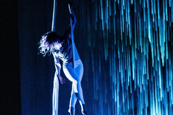 Artist performing aerial dance from suspended silks. Blue lighting cascades in the backdrop.