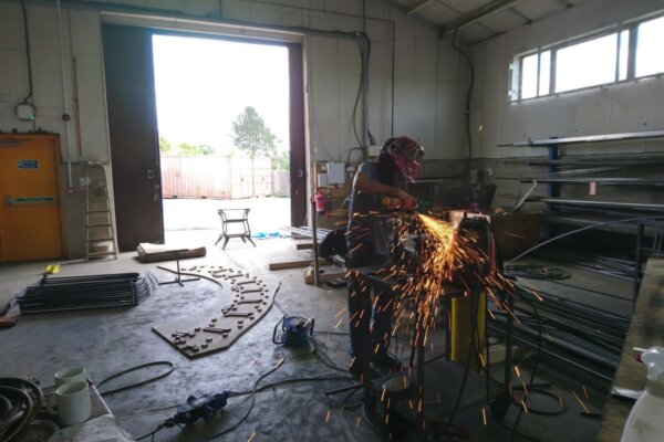 A person holds a tool, sending orange sparks flying, in the fabrication workshop at 101.