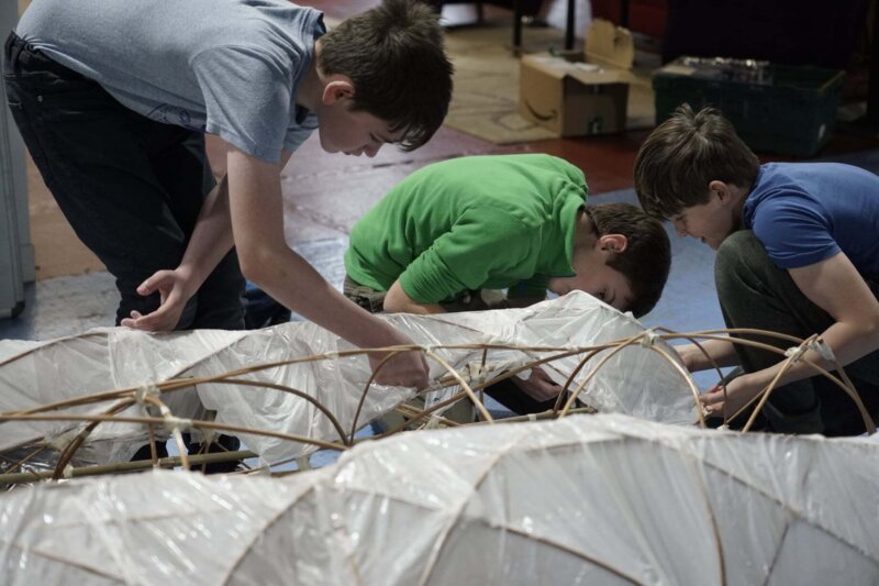 A group of boys are making a structure out of willow and paper