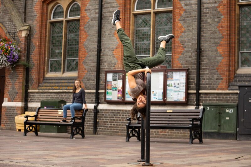 A female dancer hangs upside down from a railing in the middle of Newbury market place