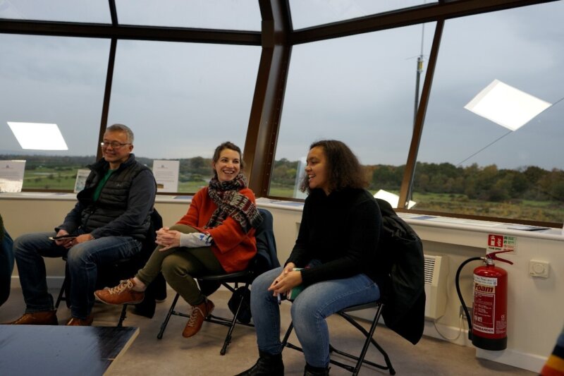 A group of people sitting inside the control tower talking and smiling.