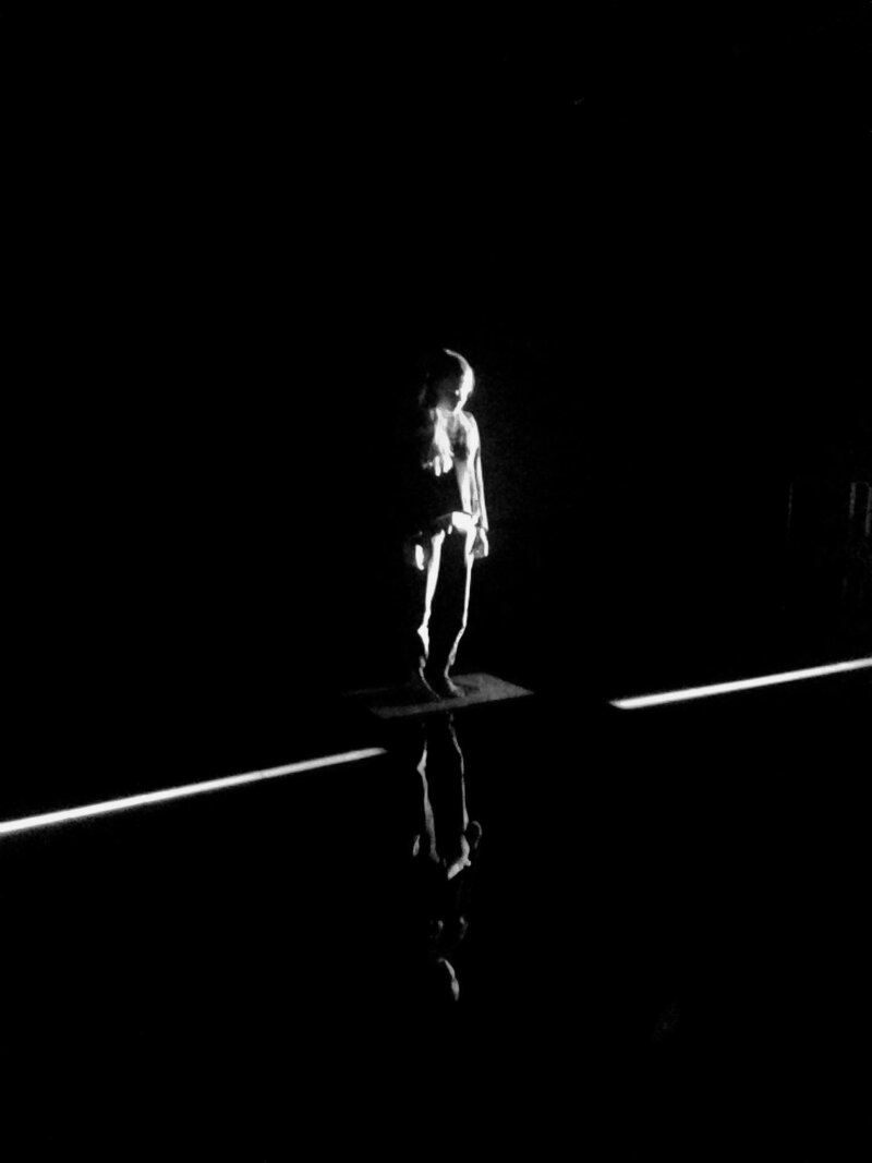 A person stands in a dark black room with a stripe of white light running across the floor.