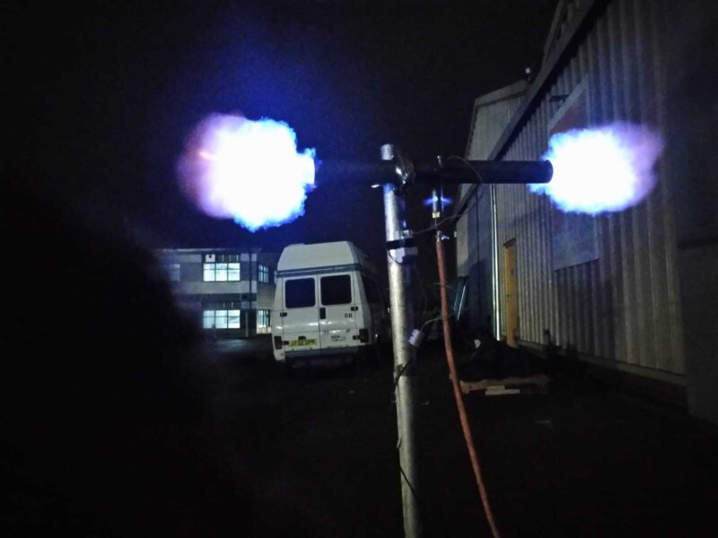 Image of pyrotechnics displaying a blue/white fire that is coming out of some metal tubing which is mounted into a pole outside of 101 building at night.